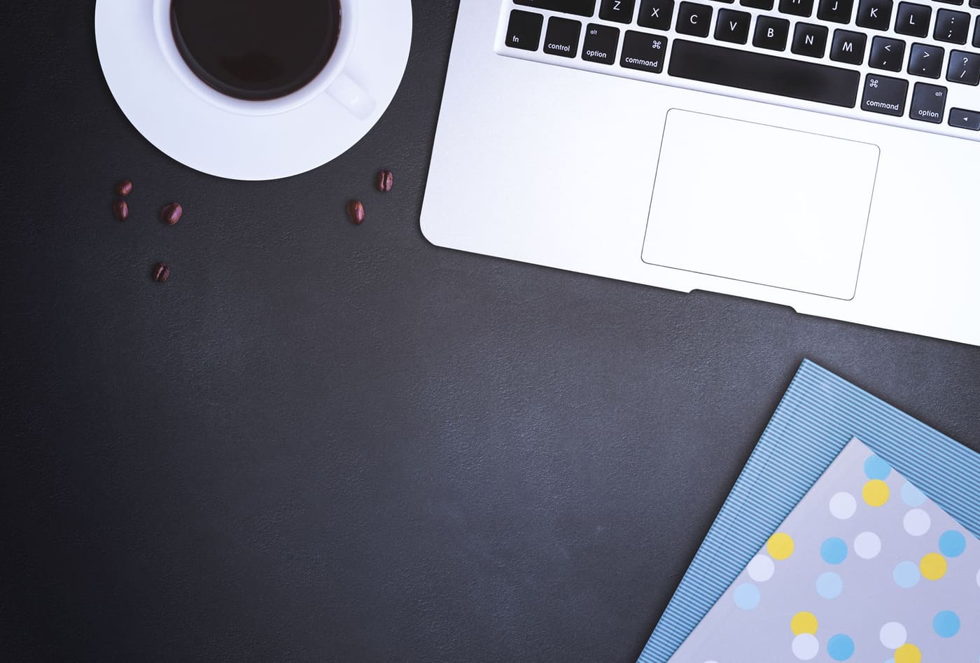 A laptop, coffee cup and papers on a dark desk seen from above