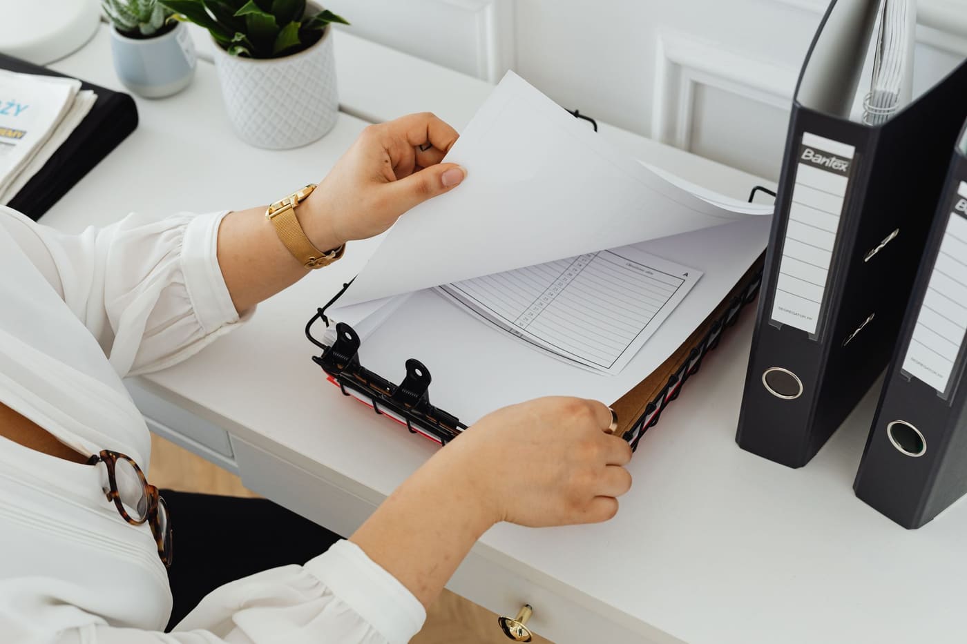 A person filing a sheet of paper into an open binder at a white desk