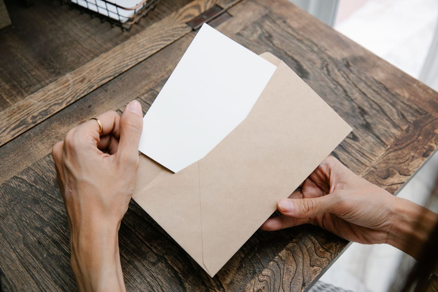 Two hands pulling a blank sheet of paper out of a brown envelope on a wooden table