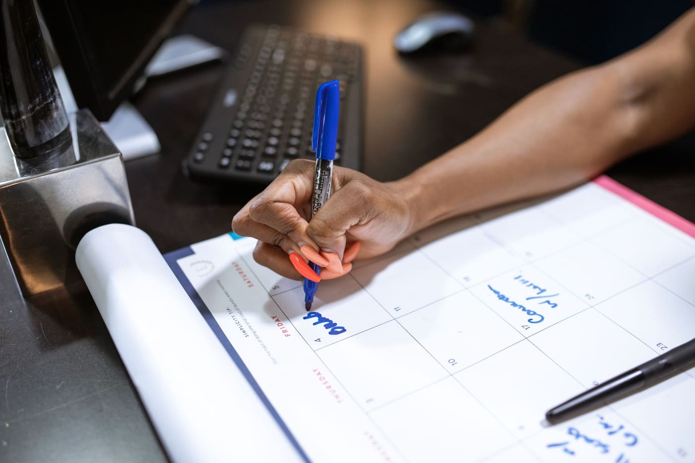 A hand writing a date on a desk calendar with a blue marker