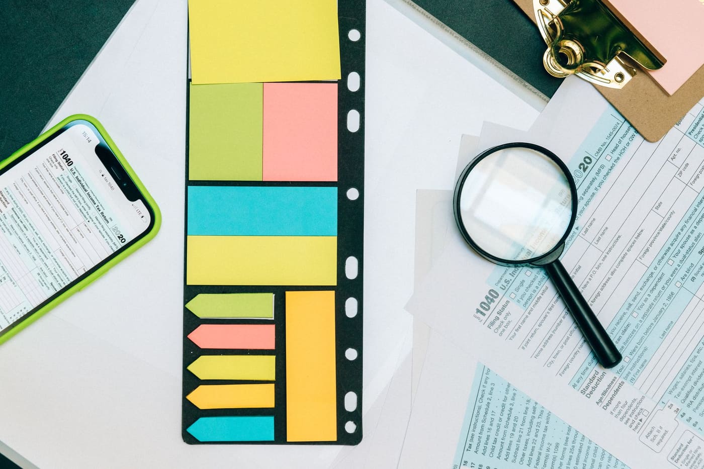 Tax forms with a magnifying glass, sticky notes and a phone on a desk