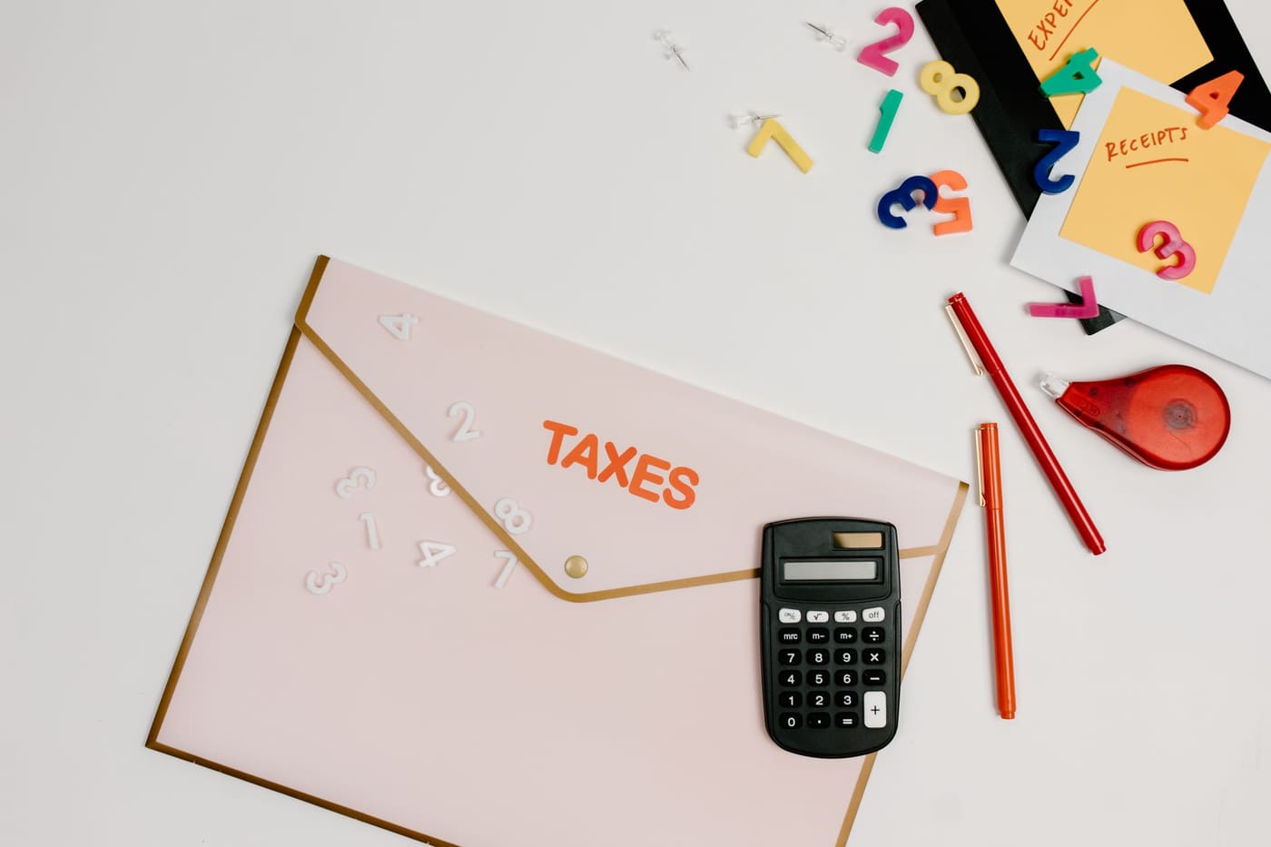 A tax folder, calculator, pens and colored number tiles on a white desk