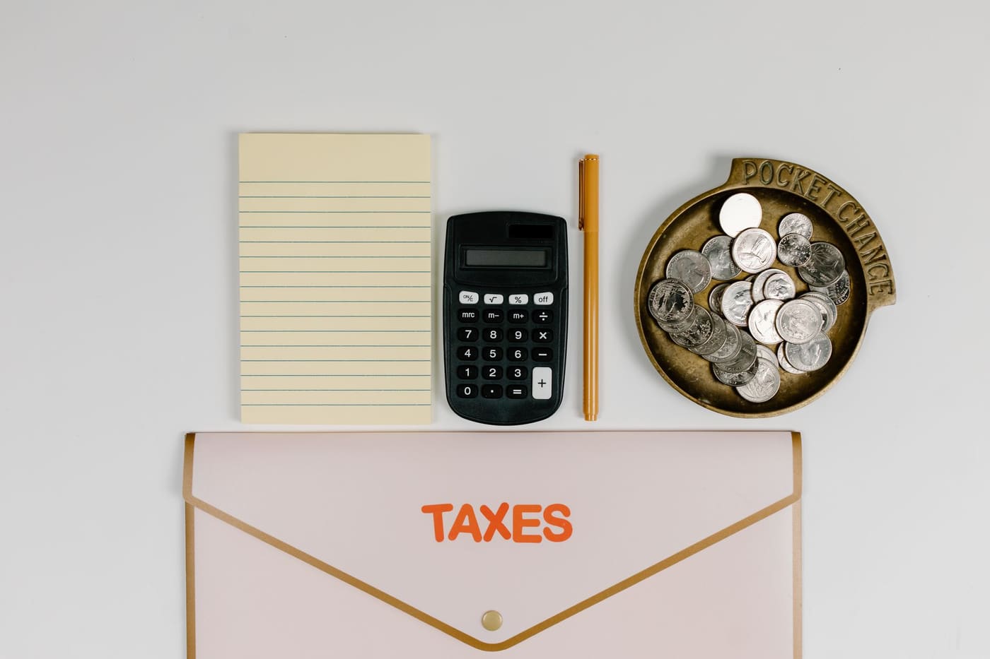 A folder marked taxes with a calculator, notepad and a dish of coins